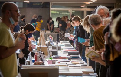Viele Menschen an einem langen Tisch stehend, auf dem Bücher liegen, die sie ansehen