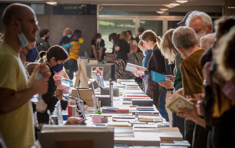 Viele Menschen an einem langen Tisch stehend, auf dem Bücher liegen, die sie ansehen