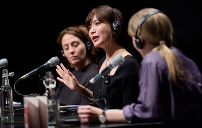 Mieko Kawakami gestikulierend und sitzend vor einem Mikrofon