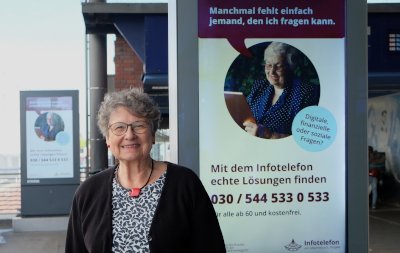 Margret Hampel vor Werbedisplay mit Werbung vom Infotelefon