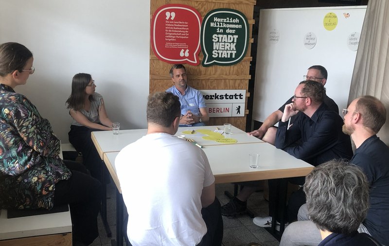 8 Personen sitzen um einen Tisch und sprechen miteinander